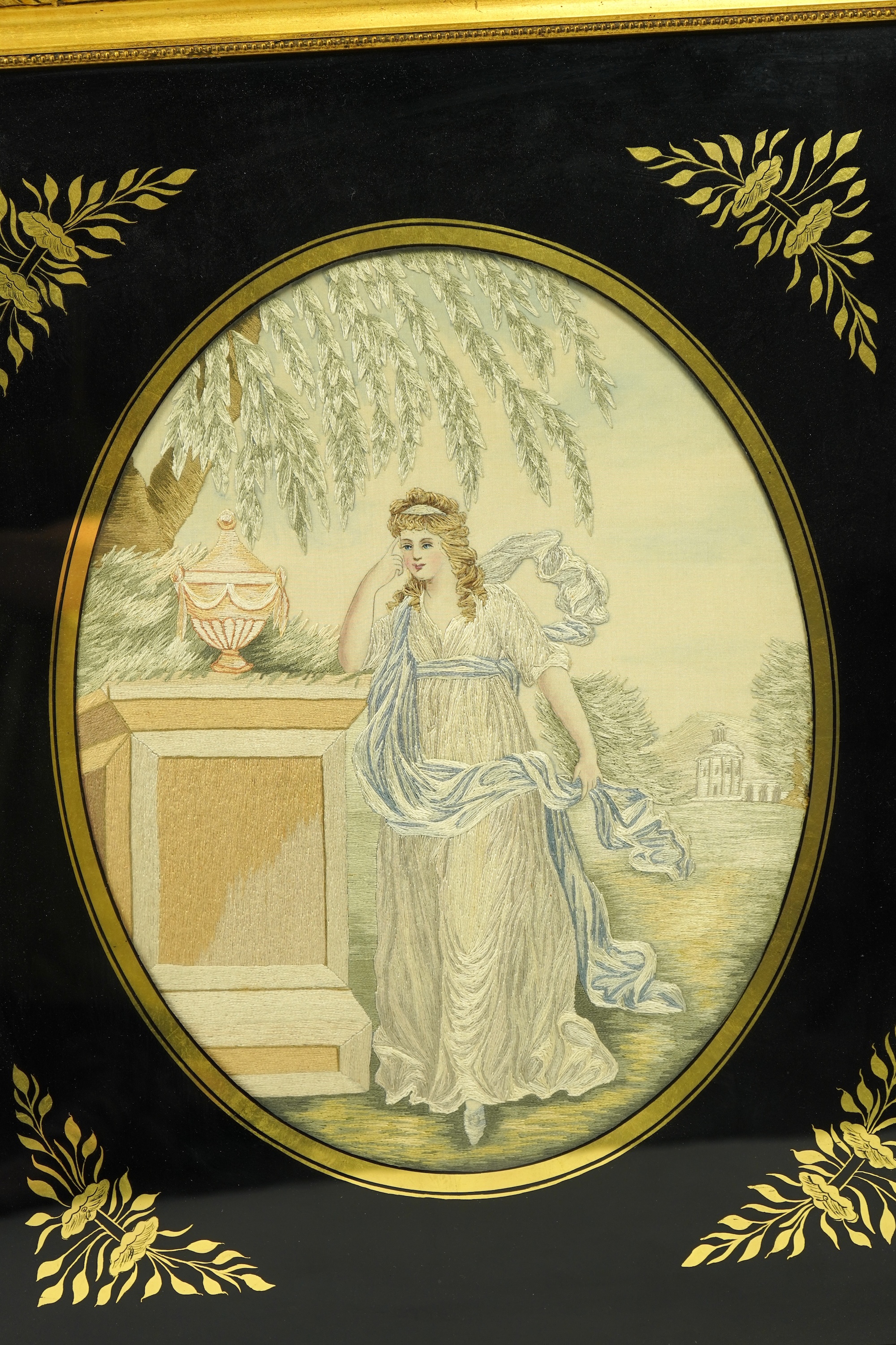 A pair of early 20th century oval silk embroideries of ladies standing by classical stone urns in a garden. Worked in pastel shades in silk using mostly stem stitch. Their faces, arms, hands and back ground silk hand pai